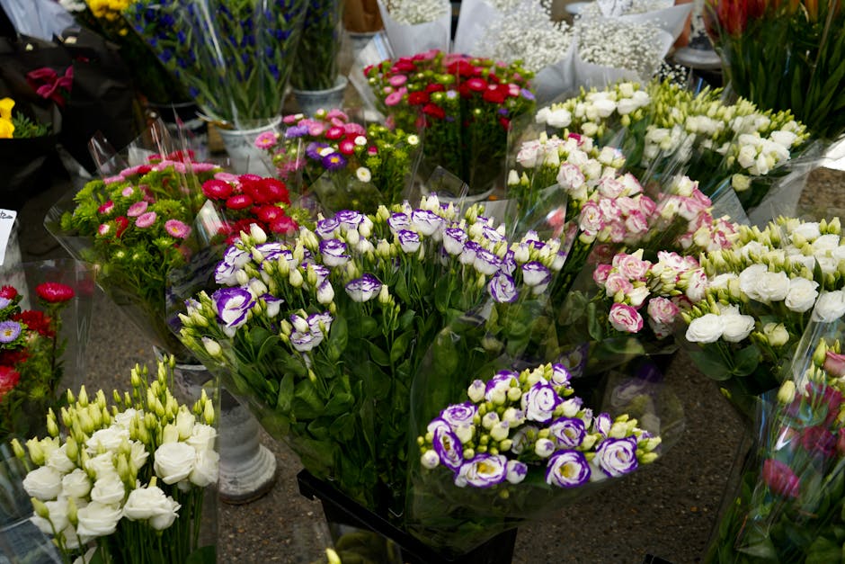 A vibrant display of fresh flowers arranged in bouquets and floral arrangements, featuring a variety of blooms including purple and white lisianthus, pink and white roses, and assorted filler flowers.