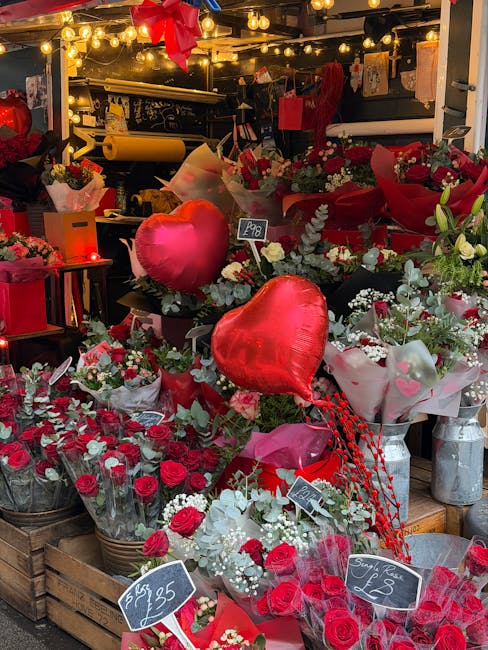 An outdoor flower display at a market stall showcases an assortment of fresh floral arrangements predominantly in shades of red, including roses, carnations, and small filler flowers, wrapped in clear
